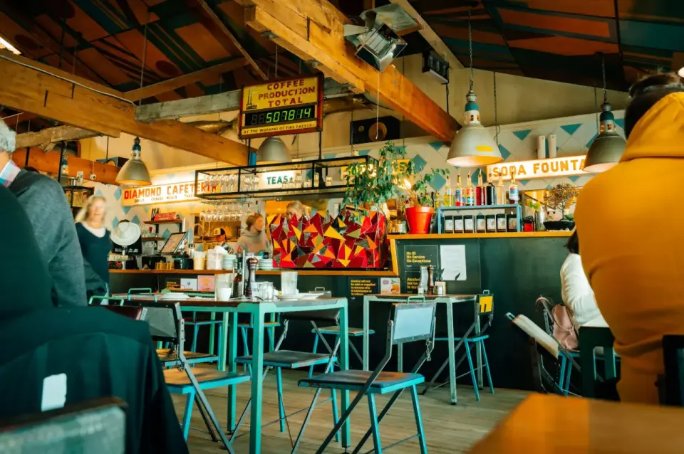 Preview of James Coleman's colourful café photograph, with turquoise stools, warm timber and a busy counter.